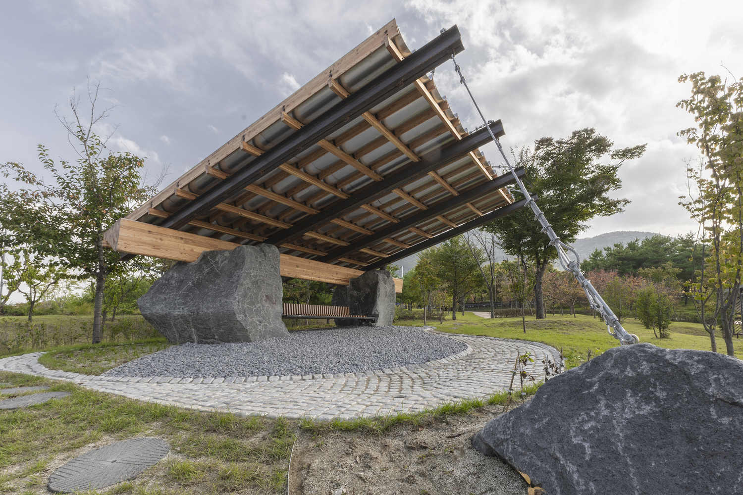 The cantilevered canopy on boulder supports under a cloudy sky with mountains in the distance