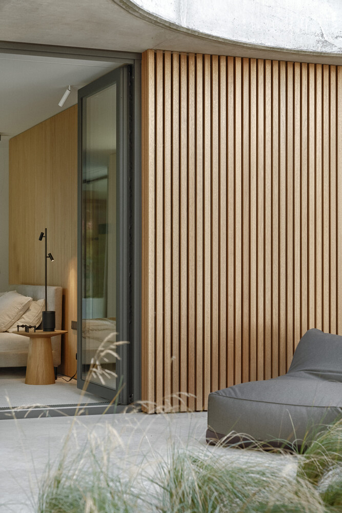 Vertical timber screen beside a sliding glass door opening to a bedroom with planted grasses in foreground