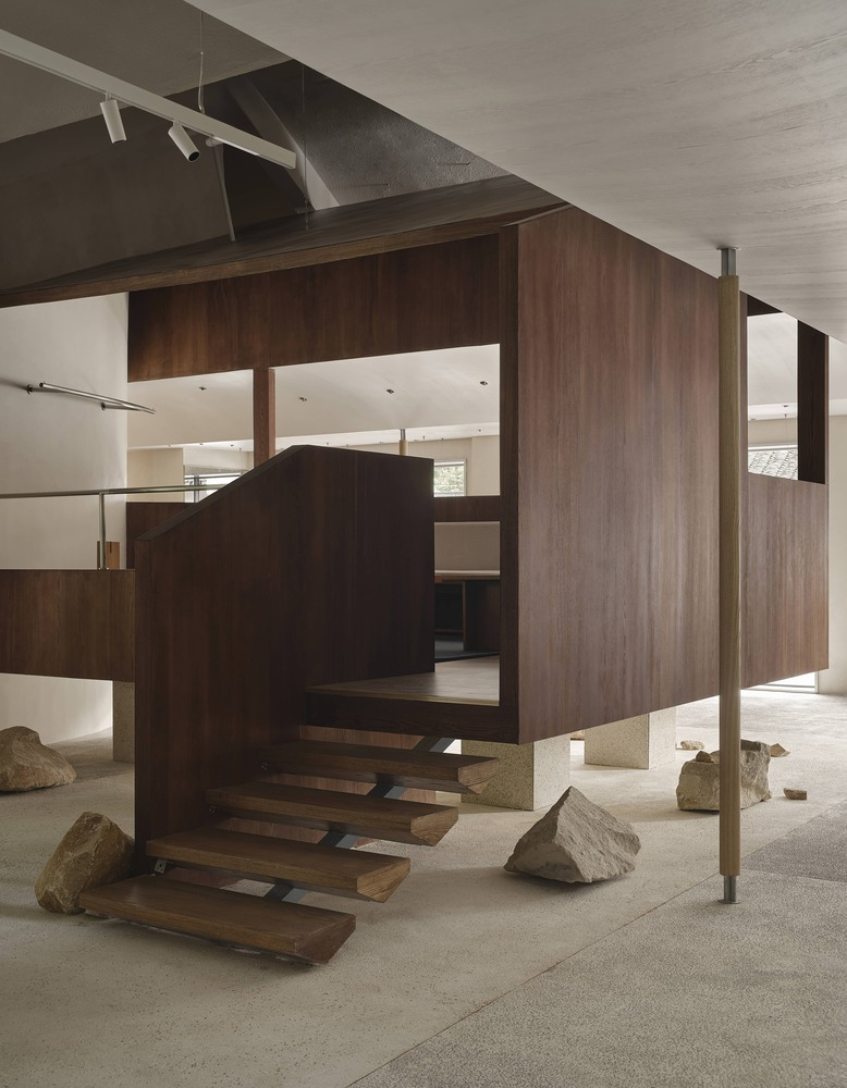 Cantilevered walnut-clad volume with floating treads and large stone boulders on polished terrazzo floor