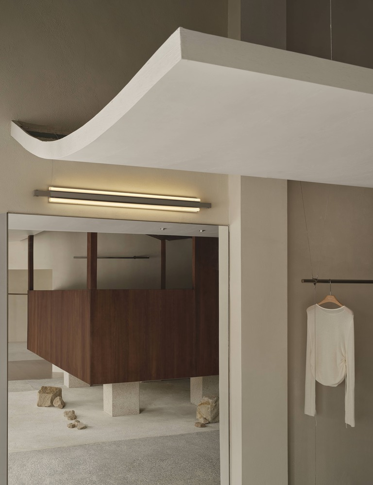 Detail of curved ceiling edge with linear light fixture above framed opening and hanging white garment