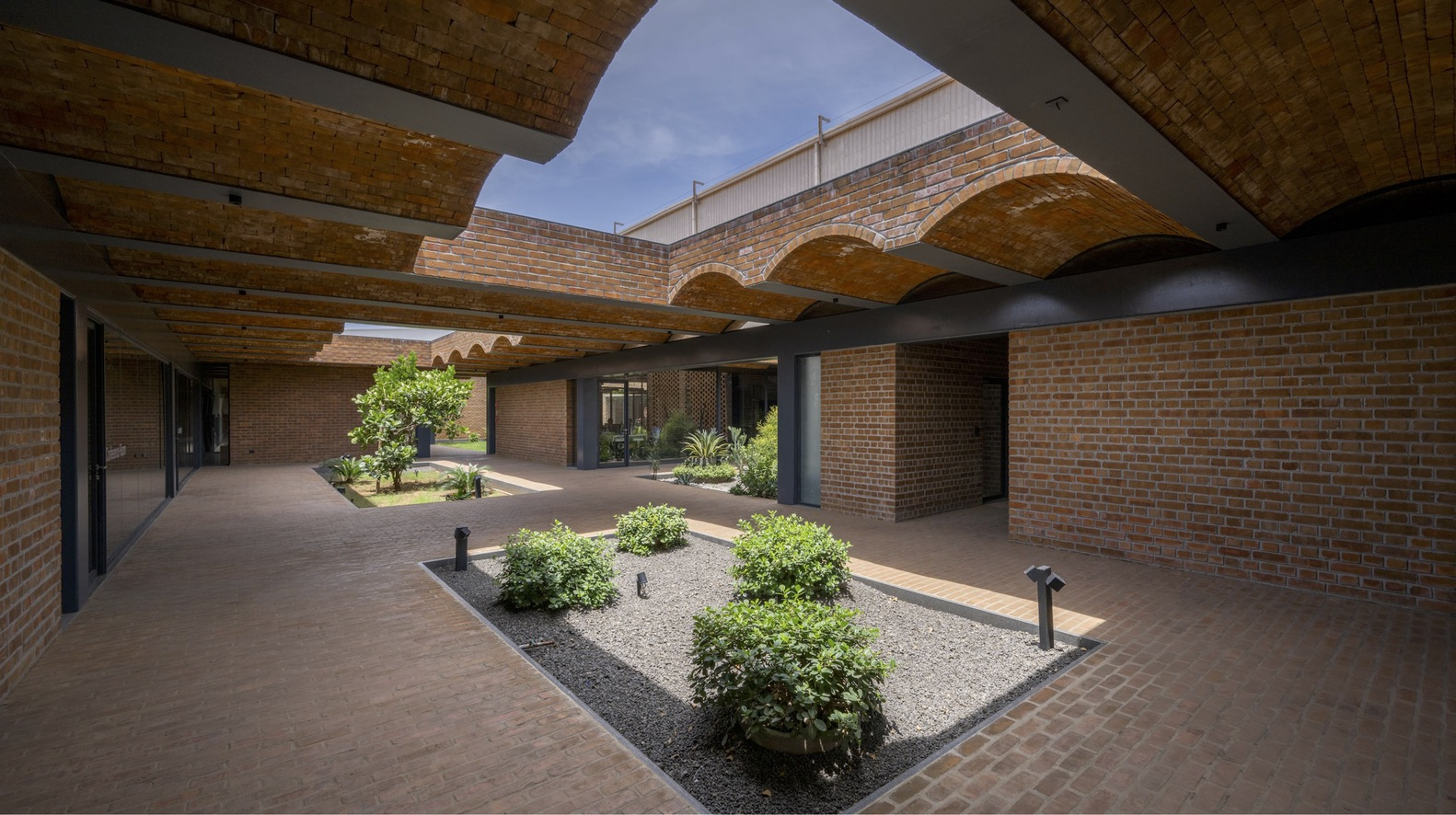 Sheltered brick courtyard with arched vaults and planted beds under a partly cloudy sky