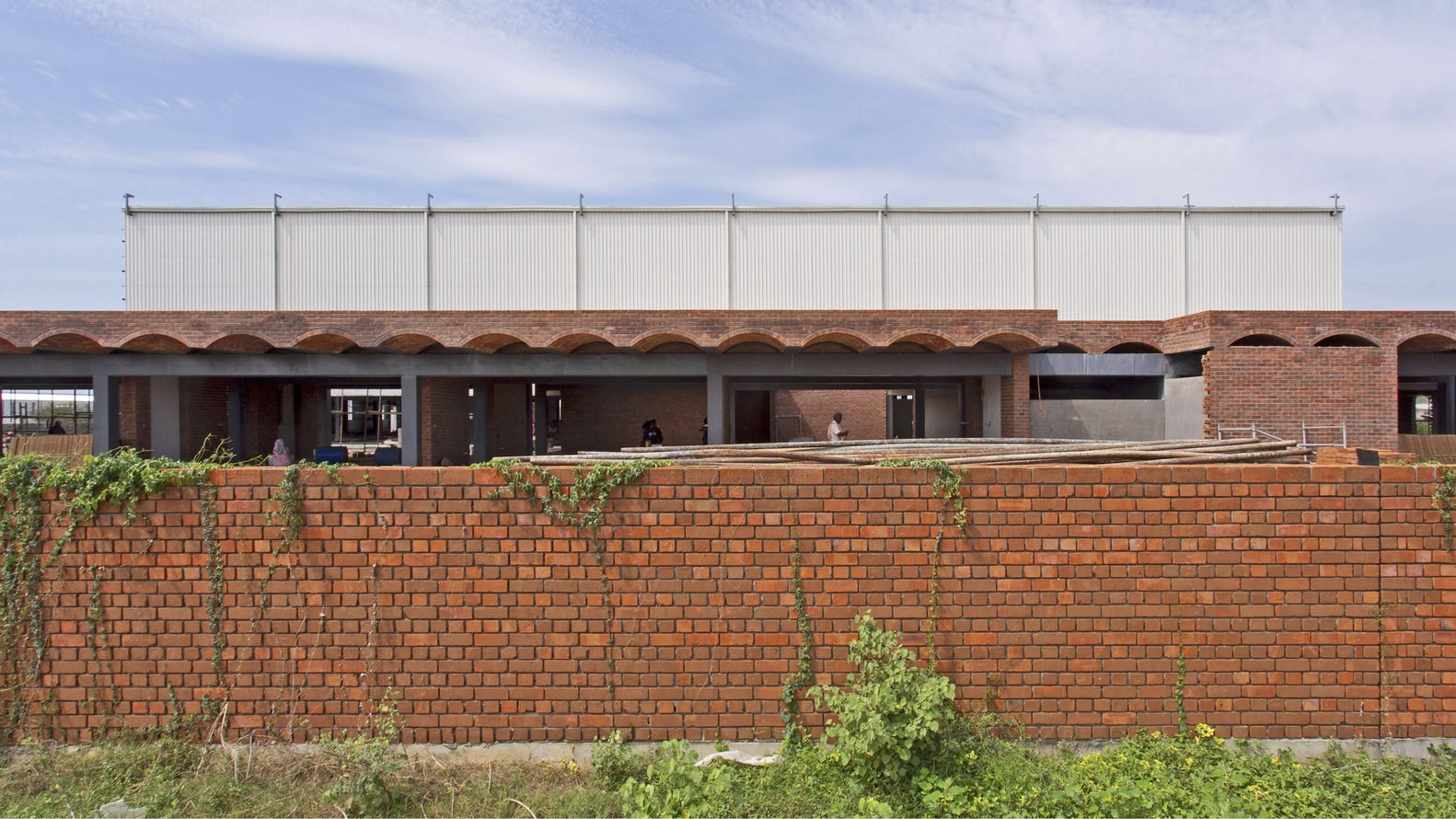 Long view of the brick boundary wall and arched colonnade with corrugated metal parapet above