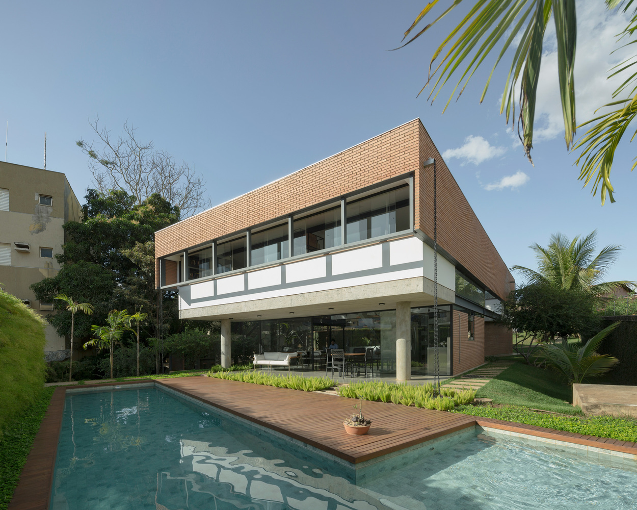 Two-story brick facade with cantilevered upper volume above pool and timber deck under palm trees