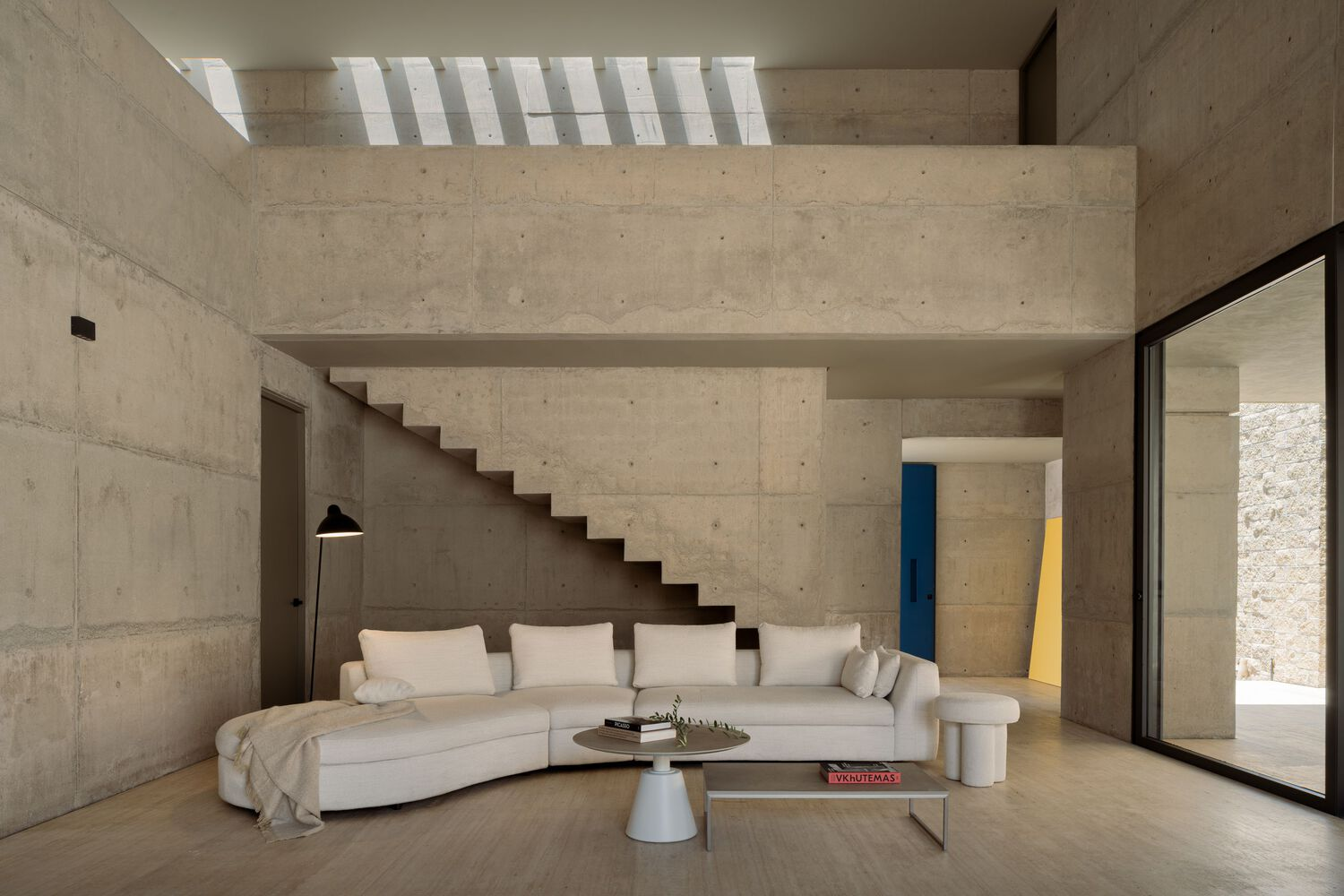 Double-height living room with cantilevered concrete staircase beneath a slatted skylight casting shadow stripes