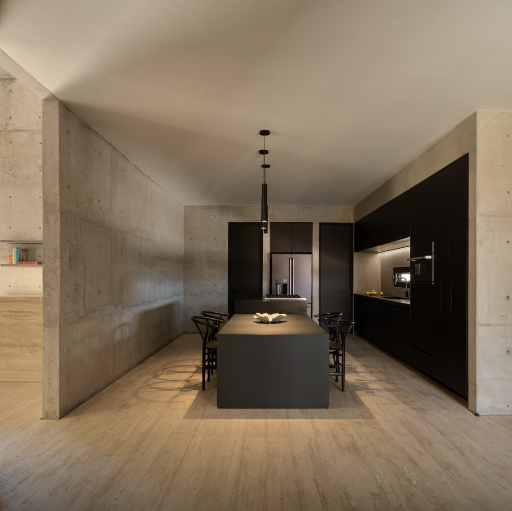 Kitchen with black island and cabinetry set between board-formed concrete columns under pendant lighting