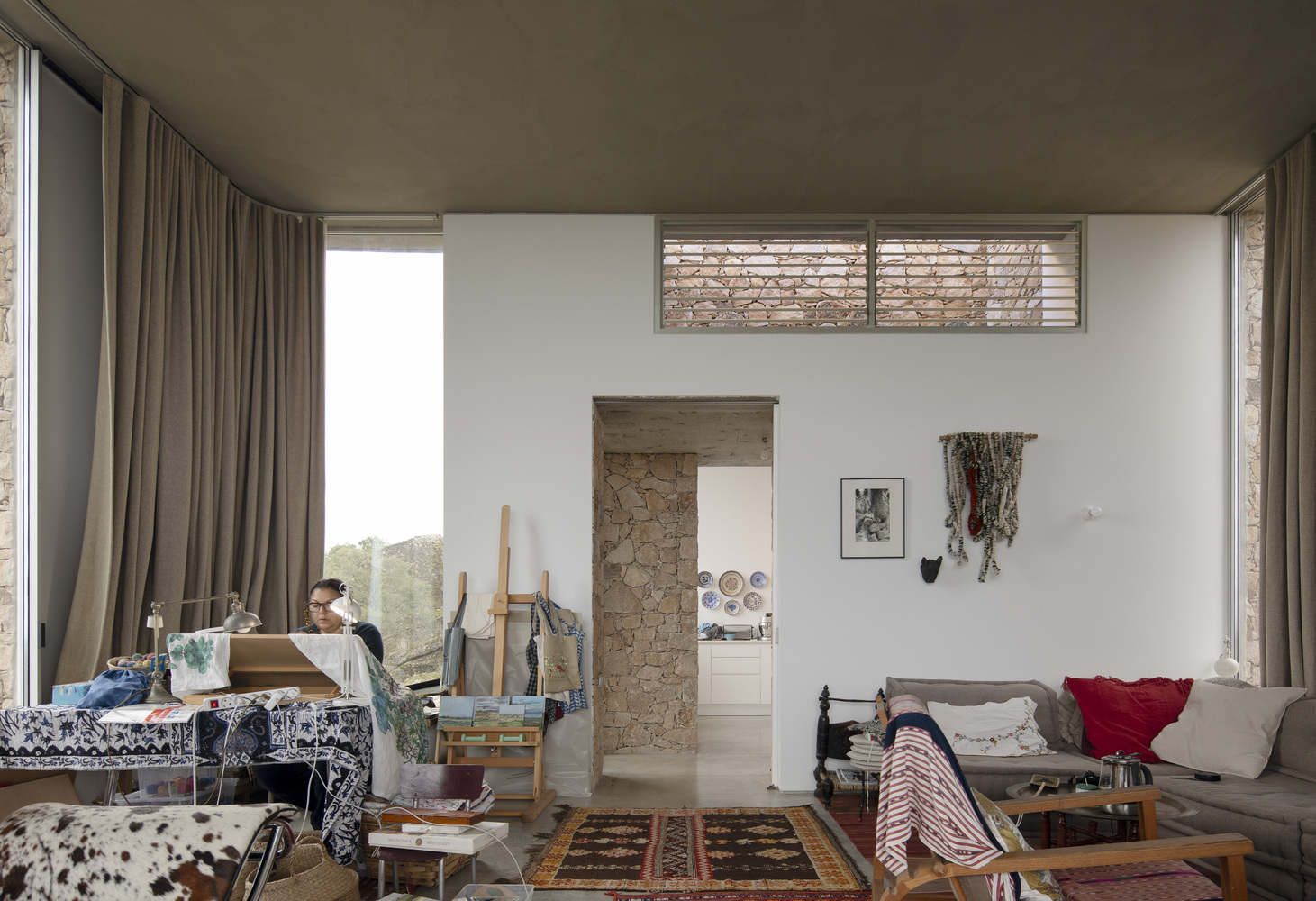 Living room interior with stone doorway, clerestory window, art studio setup and full-height curtains