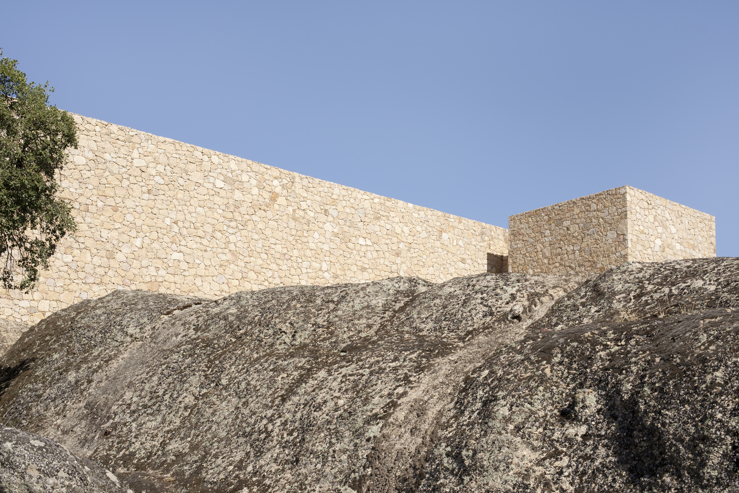 Stone volumes perched on sloped granite outcrop beneath clear sky