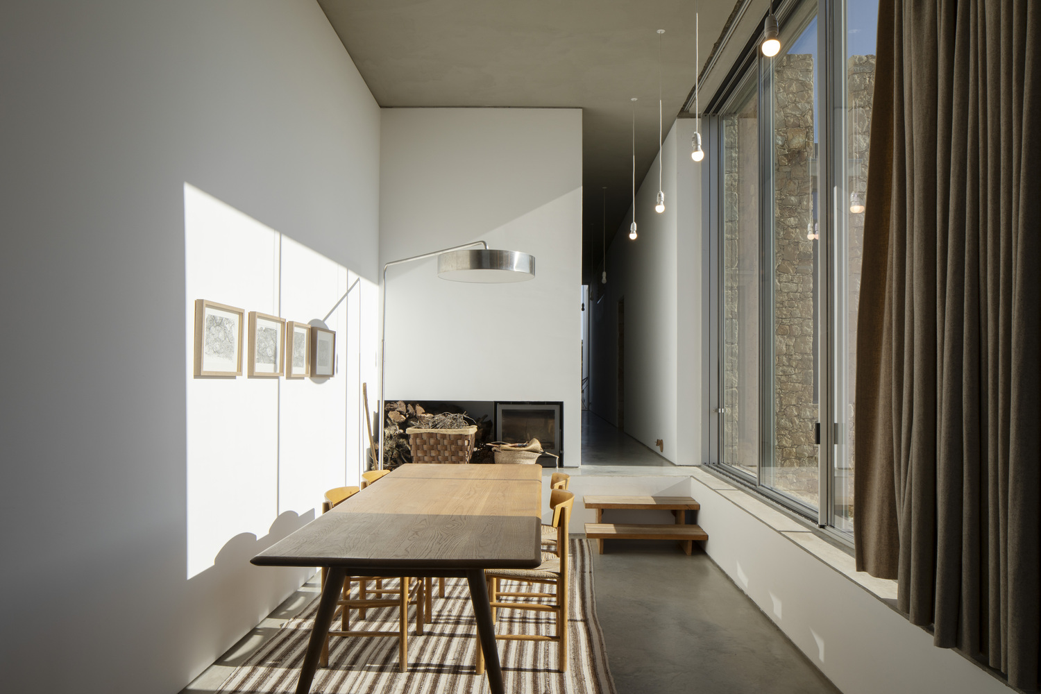 Dining space with timber table and suspended pendant lights casting shadows through glazed wall