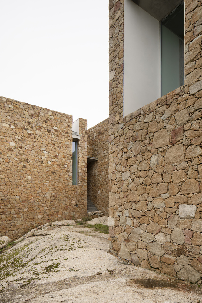 Narrow courtyard between rough stone walls with patches of grass on the sandy ground