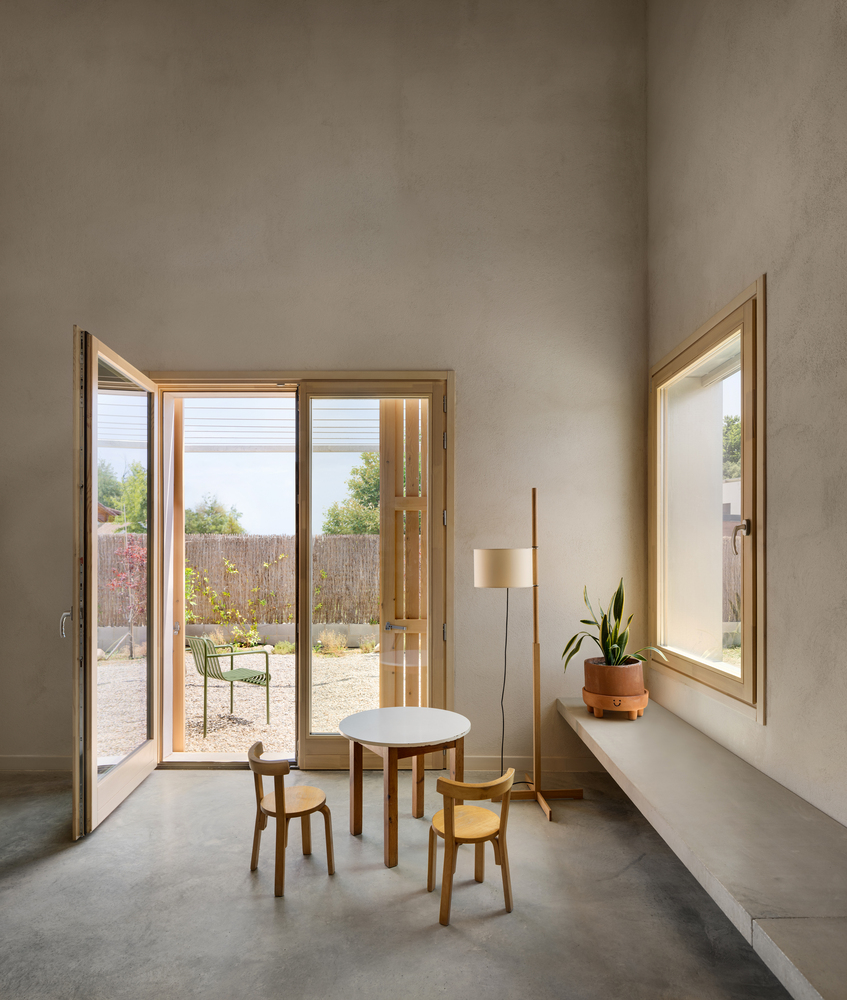 Glazed door opening to gravel courtyard with reed fence and a single round table with two stools