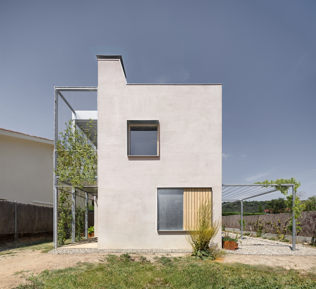 Street-facing elevation with stacked square windows on pale stucco wall and metal mesh stair tower with green climbers