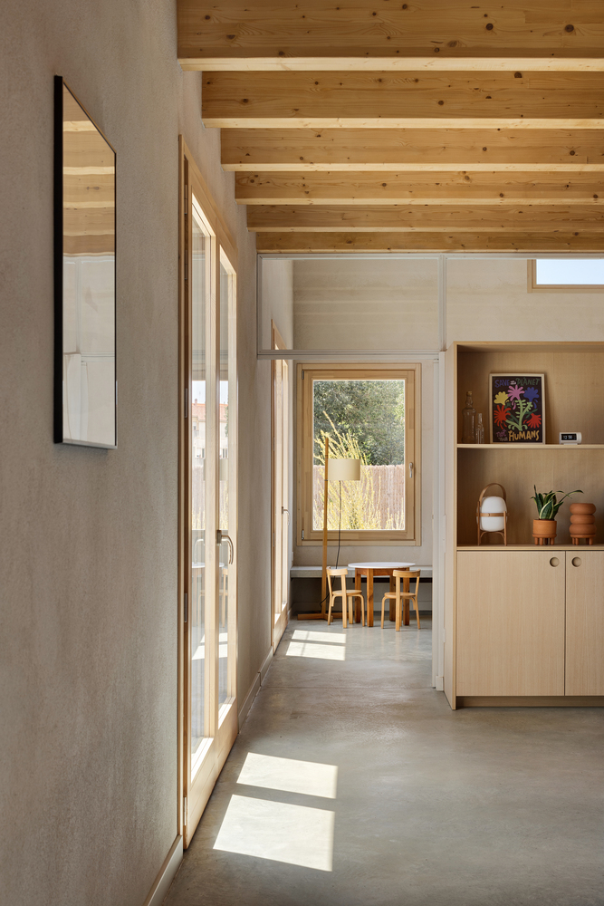 Sunlit hallway with concrete floor and timber-framed glazing casting shadows across the passage