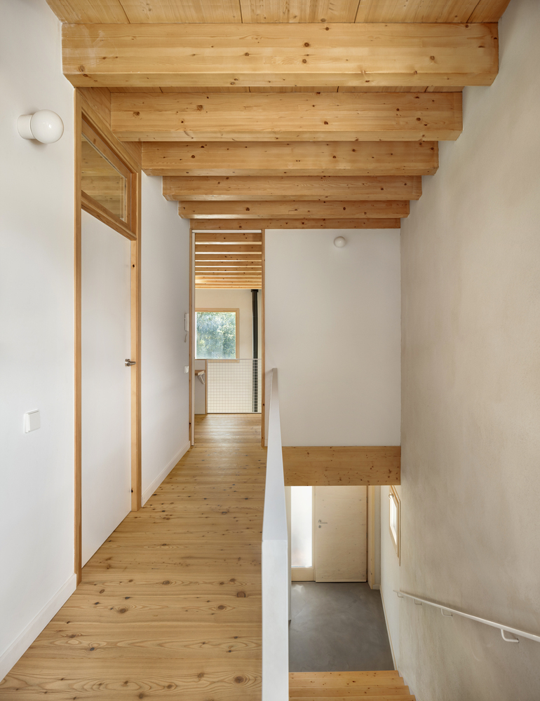 Upper level hallway with pine flooring and exposed timber beams overlooking the entry below