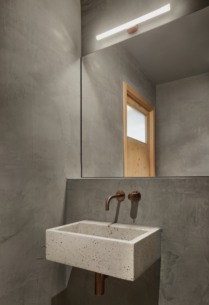 Powder room with cast concrete walls, terrazzo basin and copper fixtures under a skylight