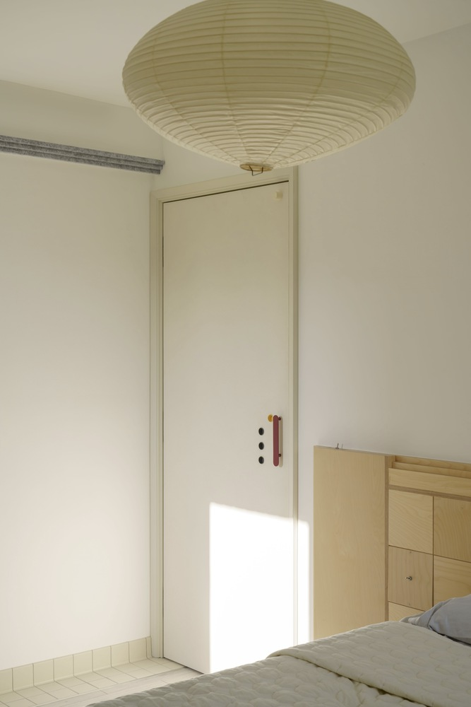 Bedroom door with maroon handle beneath a large pendant light casting sunlight across white walls