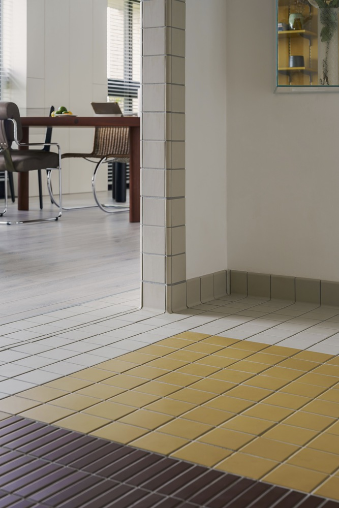 Tiled floor threshold in yellow, grey and violet tones beneath white wall and column