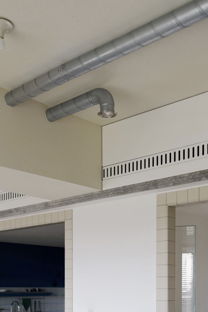 Exposed galvanized ductwork running along ceiling above ventilation grille and tiled column