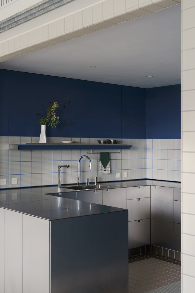 Kitchen island with stainless steel countertop beneath white square tile backsplash and navy blue upper wall