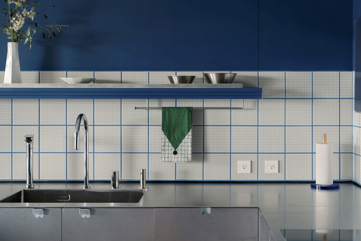 Stainless steel sink and backsplash with white square tiles accented by blue grout lines