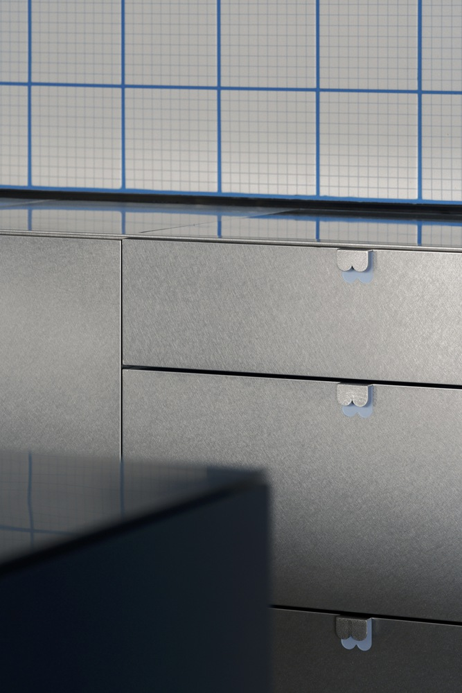 Detail of grey laminate drawer fronts with white cylindrical pulls against gridded tile backsplash