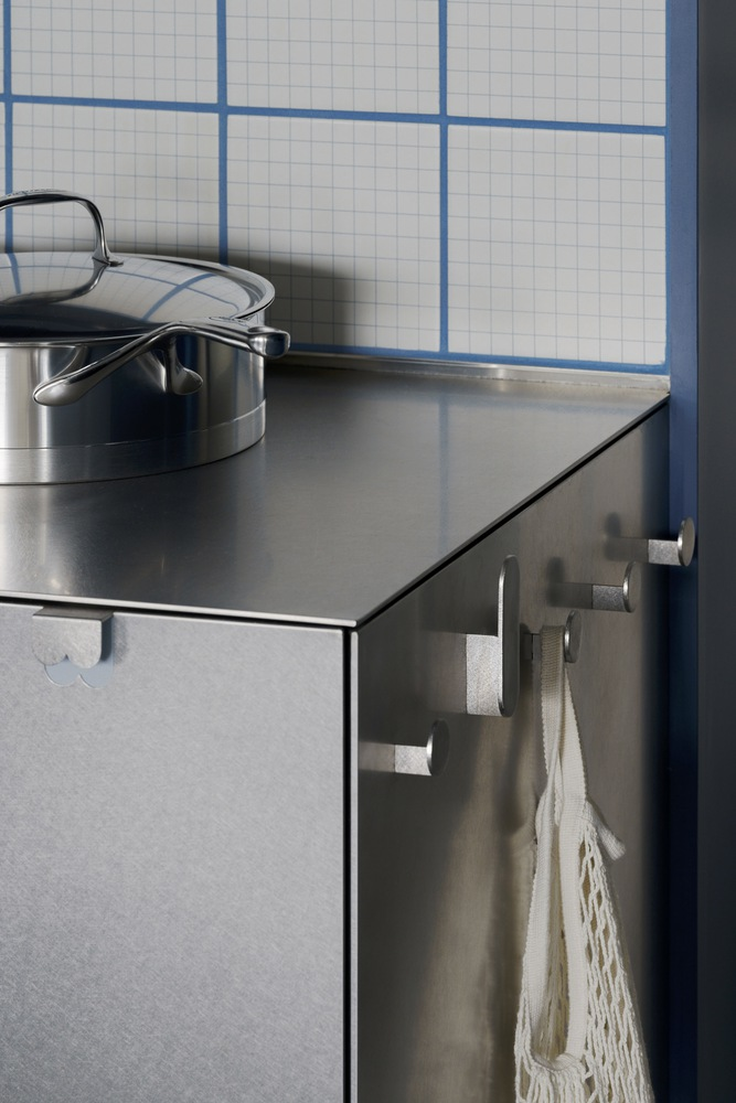 Stainless steel countertop edge with towel hook and stockpot beneath white gridded tile wall