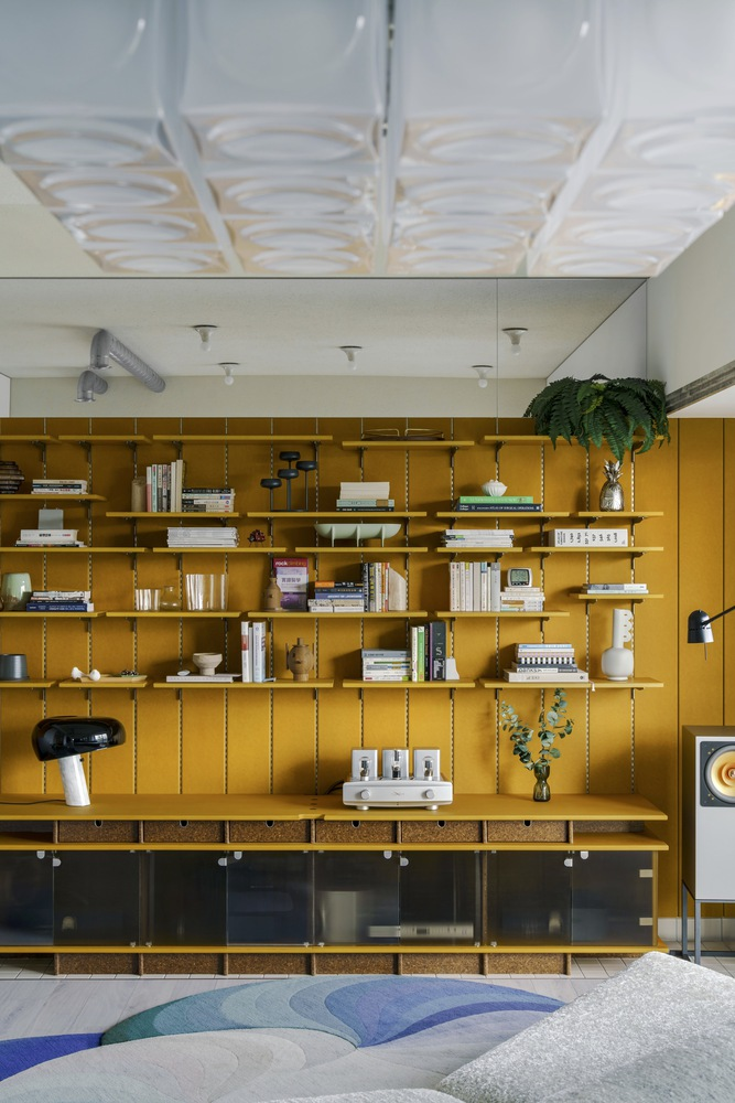 Mustard yellow shelving unit filled with books beneath an undulating white plaster ceiling