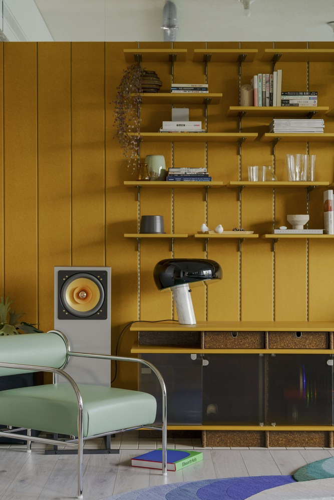 Mustard wall unit with chain-hung shelves displaying books and ceramics beside a tubular chrome chair