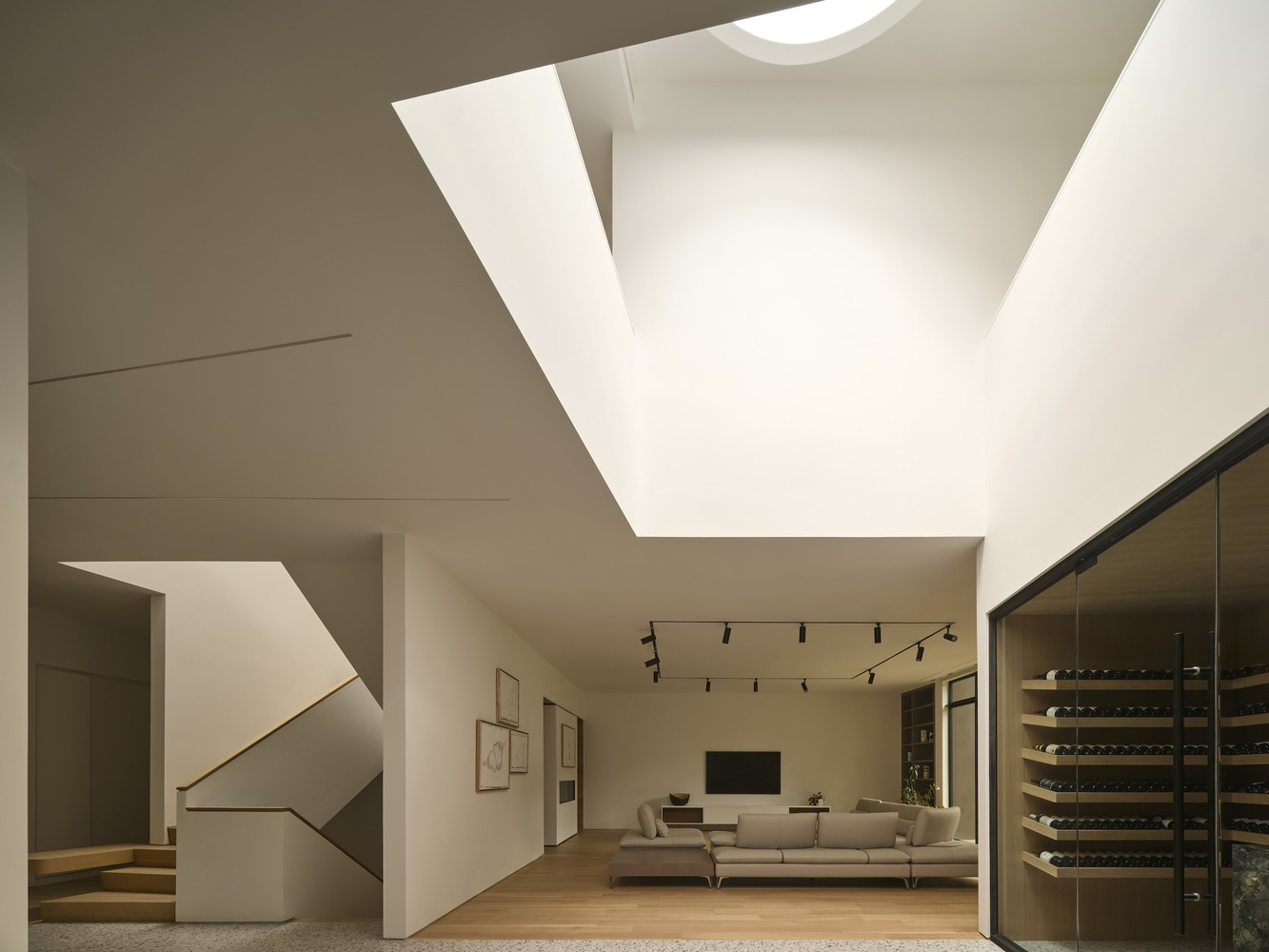 Living room with angular skylights and a floating geometric ceiling plane above white walls