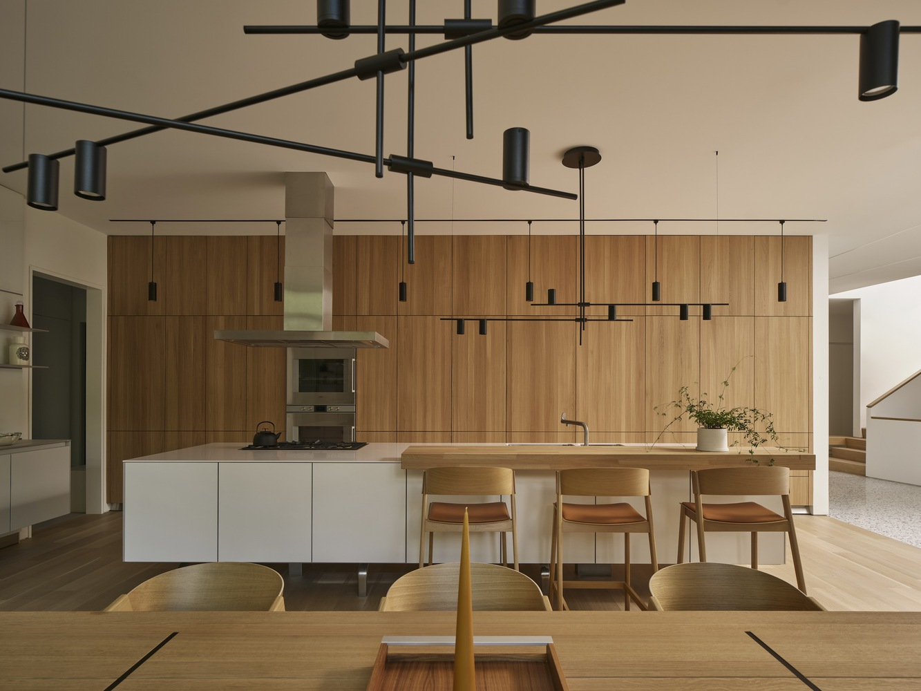 Open kitchen with timber cabinetry, white island, and suspended black track lighting fixtures