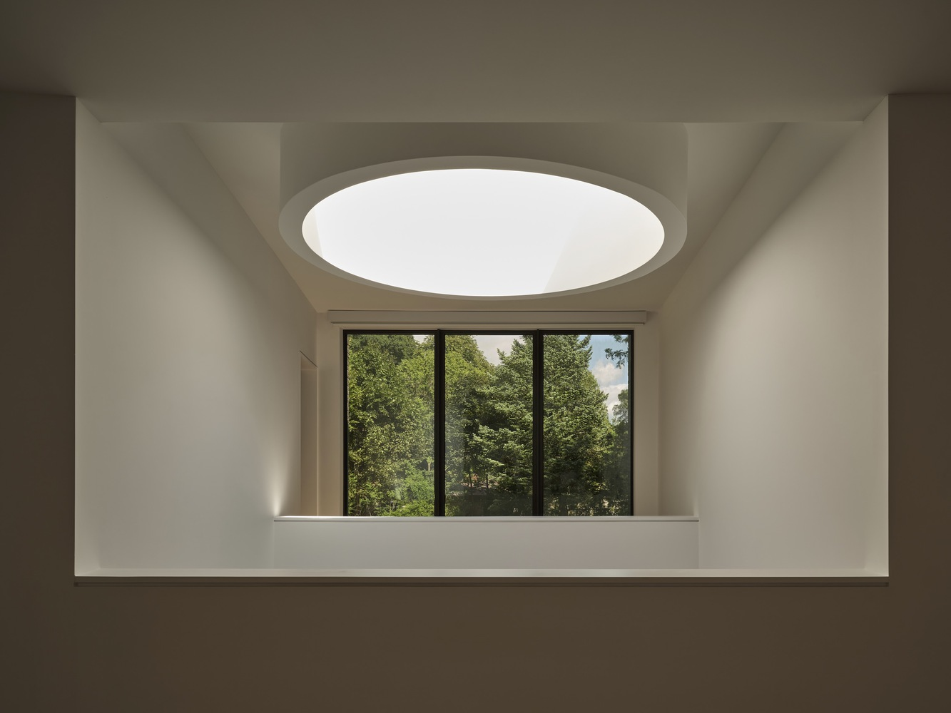 Interior niche with horizontal window framing garden view and circular skylight above