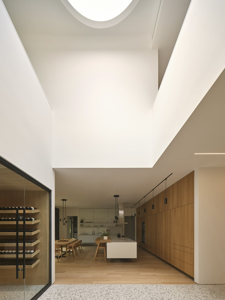 Double-height kitchen space with circular skylight above timber cabinetry and terrazzo flooring