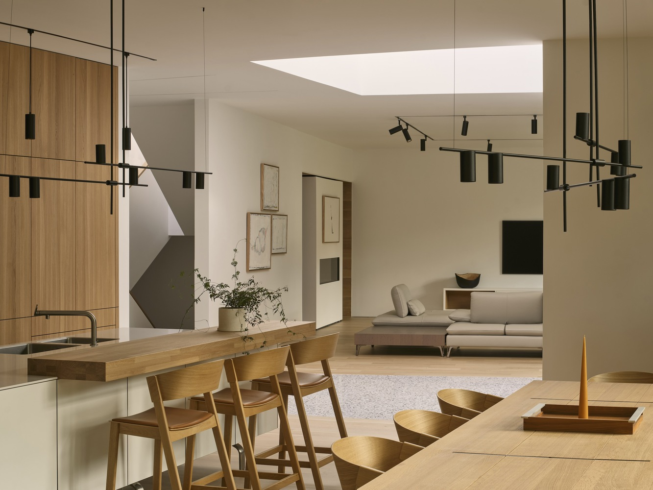 Open-plan interior with timber dining bar and suspended track lighting beneath a rectangular skylight