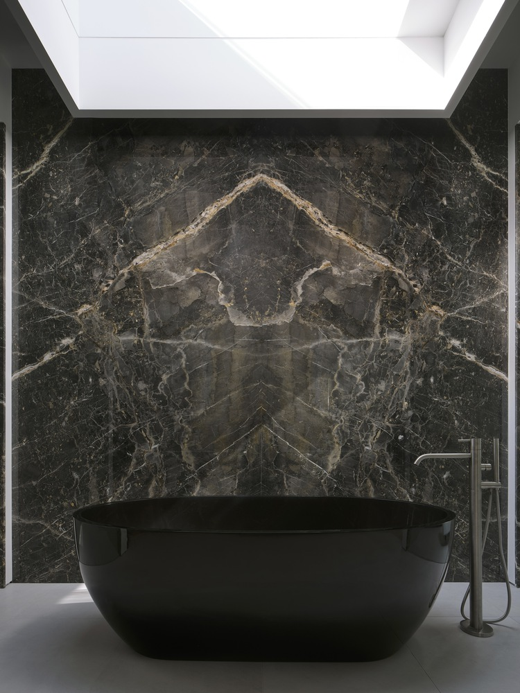 Freestanding black bathtub against a bookmatched dark marble wall beneath a recessed skylight
