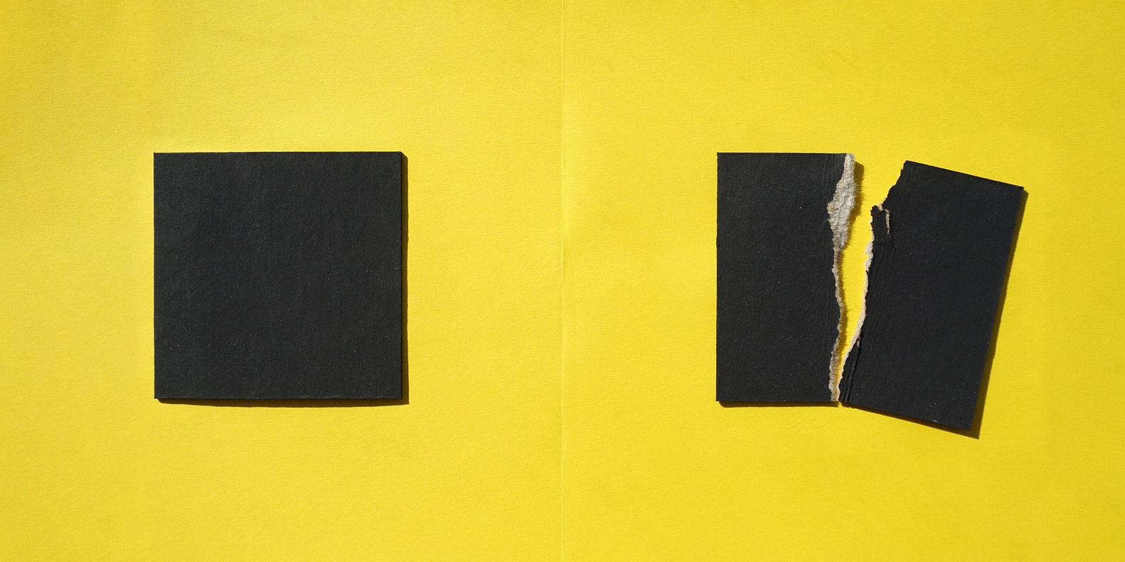 Close-up of yellow wall surface with two black square openings showing torn edges