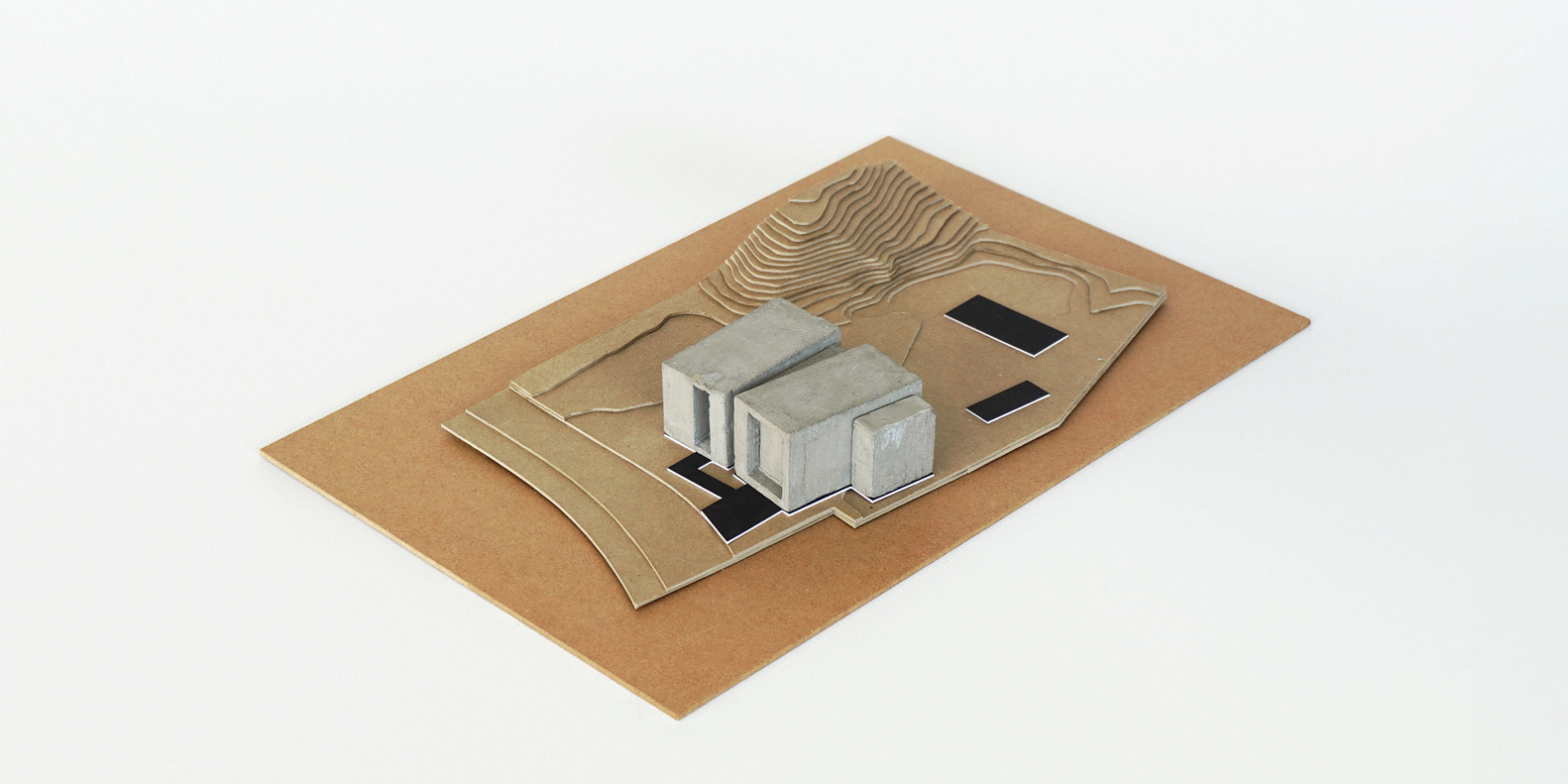 Physical model on cardboard base showing concrete volumes amid carved topographic contours