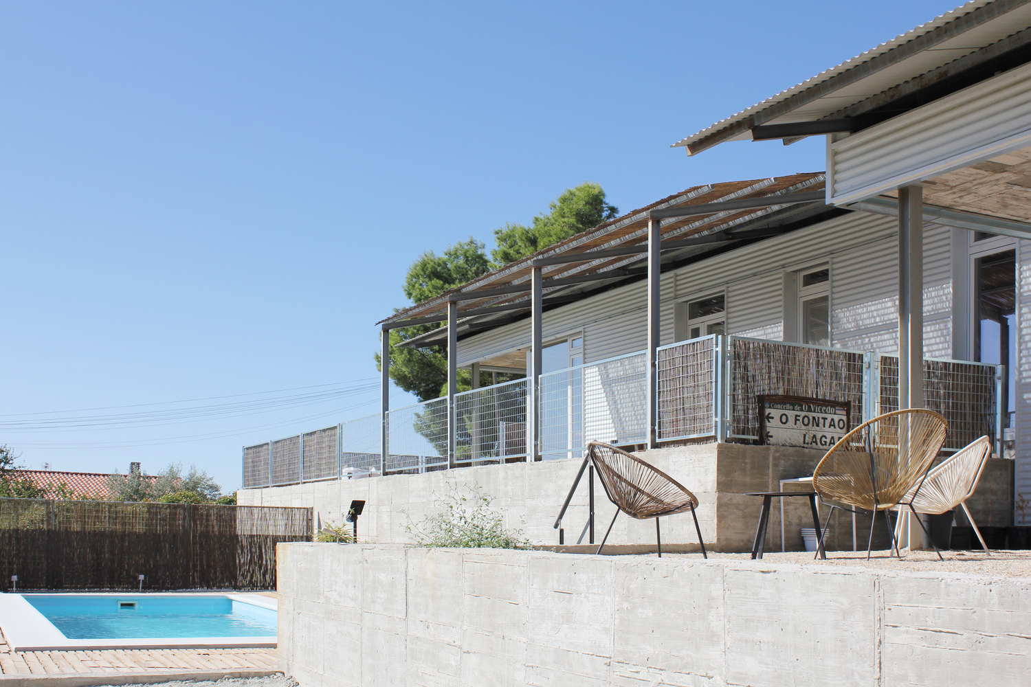 Concrete terrace with woven chairs overlooking a swimming pool and horizontal cane privacy screen