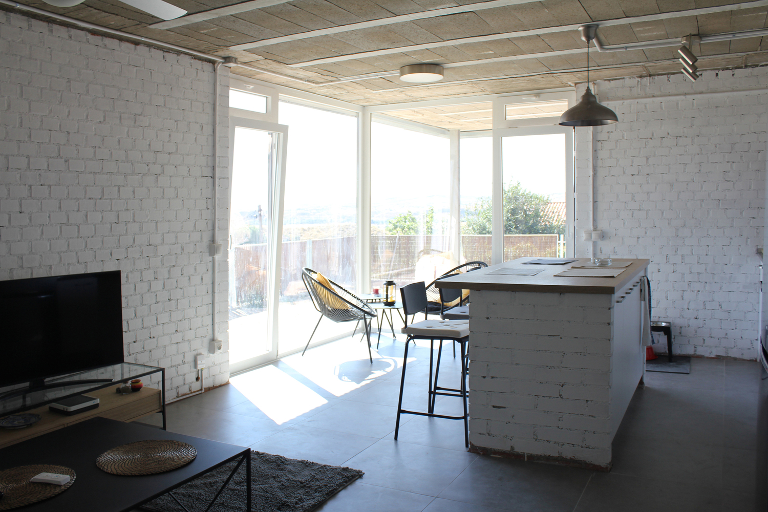 Interior with painted brick walls and timber ceiling opening to glazed doors and terrace beyond