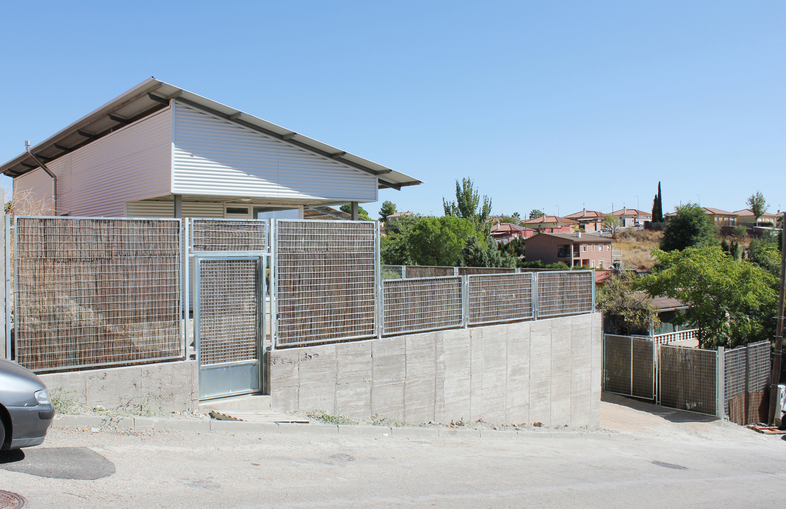 Entry gate set into concrete wall with metal mesh panels and hillside neighborhood beyond