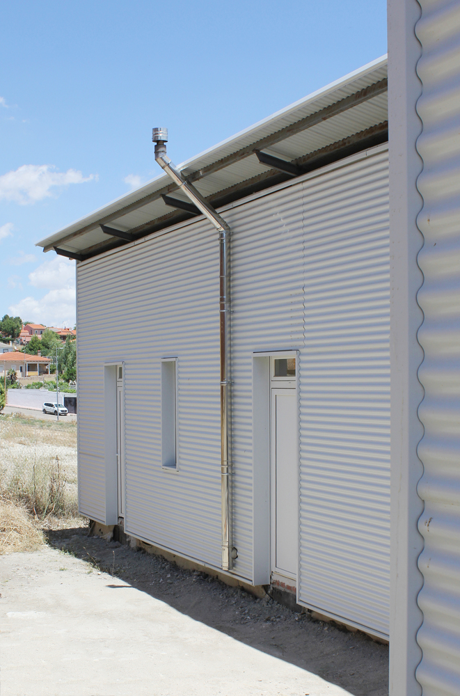Corner facade of white corrugated metal cladding with vertical window slots and rooftop vent