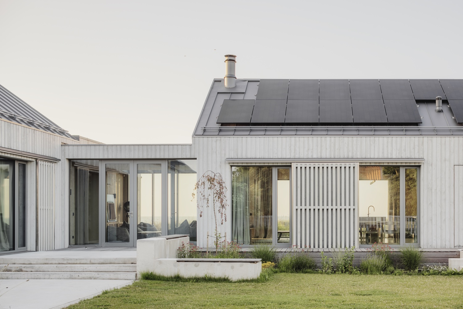 Rear terrace with vertical metal cladding, sliding glass doors, and solar panels on the pitched roof