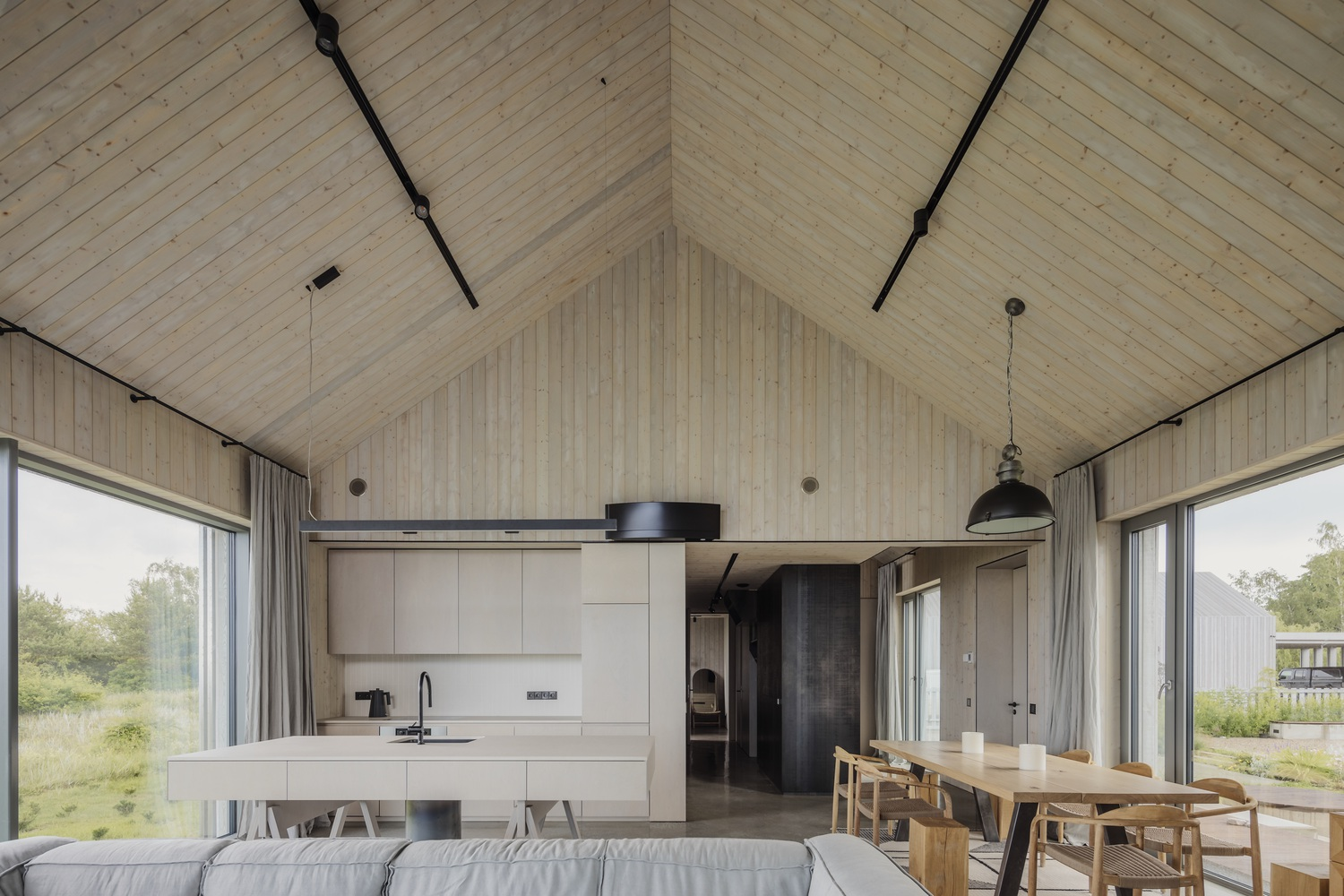 Open-plan living space with vaulted tongue-and-groove ceiling, black track lighting, and kitchen island