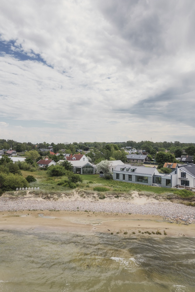 Aerial view of the metal-roofed residence along a pebble beach with neighboring houses inland