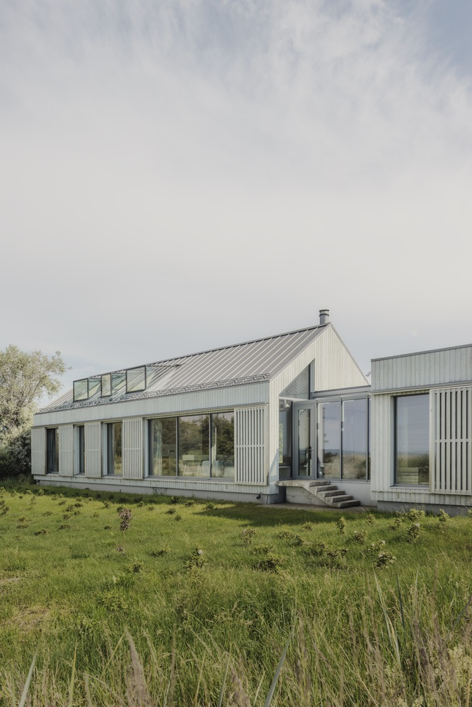 Garden-facing elevation with glass doors, timber cladding, metal roofing and skylights in overcast light
