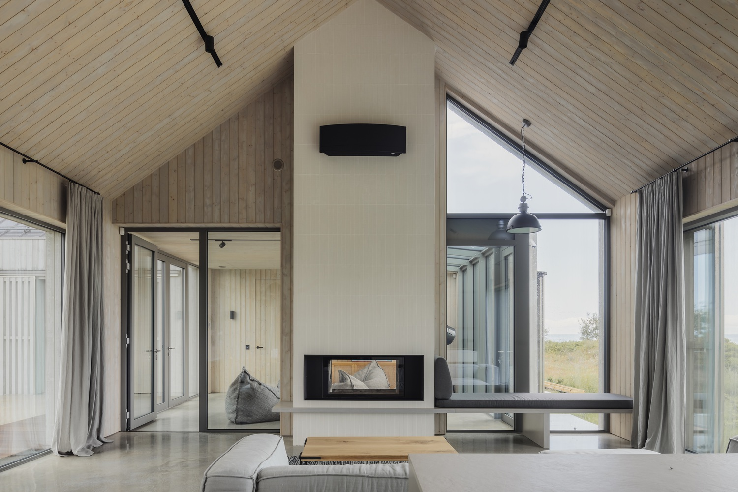 Living room with freestanding white fireplace core, timber-lined vaulted ceiling and full-height glass doors