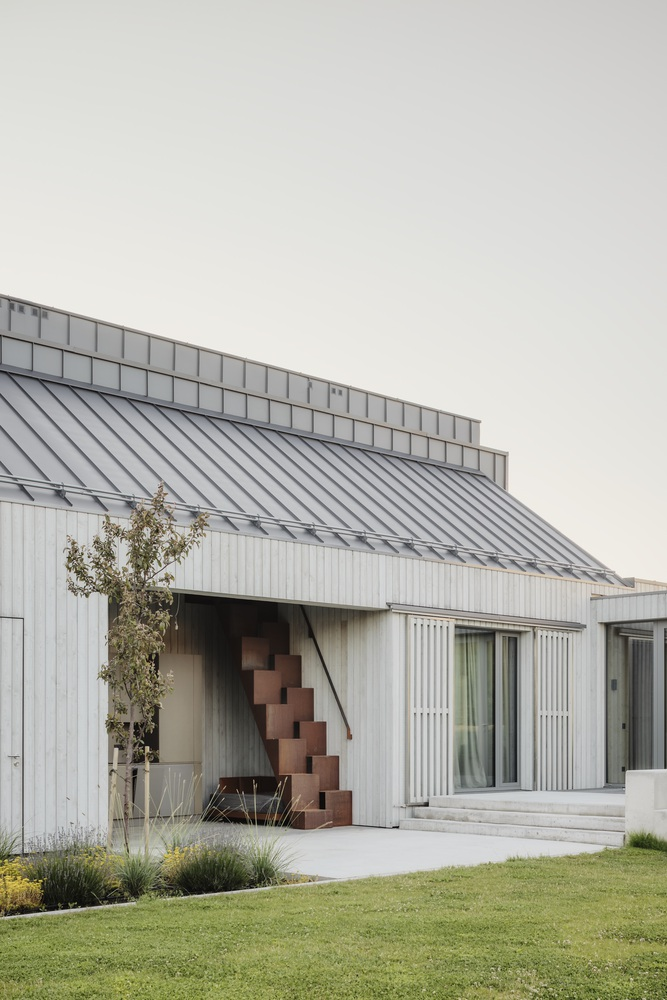 Courtyard corner showing stacked terracotta masonry element framed by vertical timber cladding and metal roofing