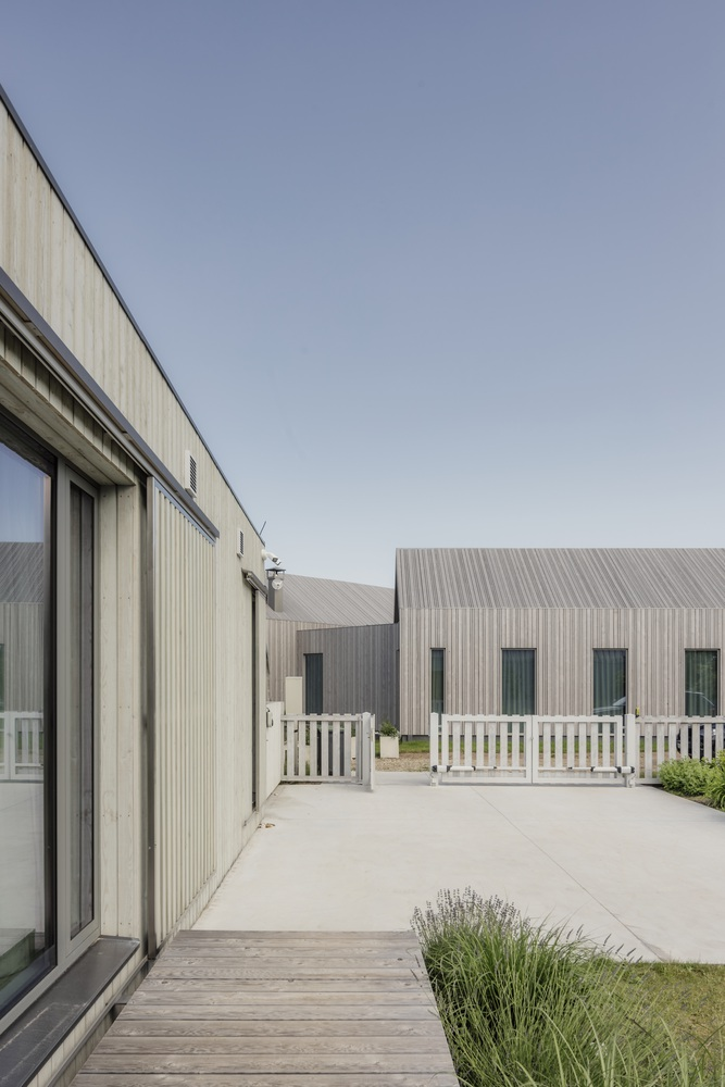 View across timber deck to corrugated metal facade and white painted fence enclosing paved courtyard