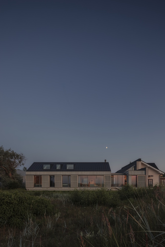 Facade of the timber-clad residence with vertical shutters and skylights at dusk with moon overhead