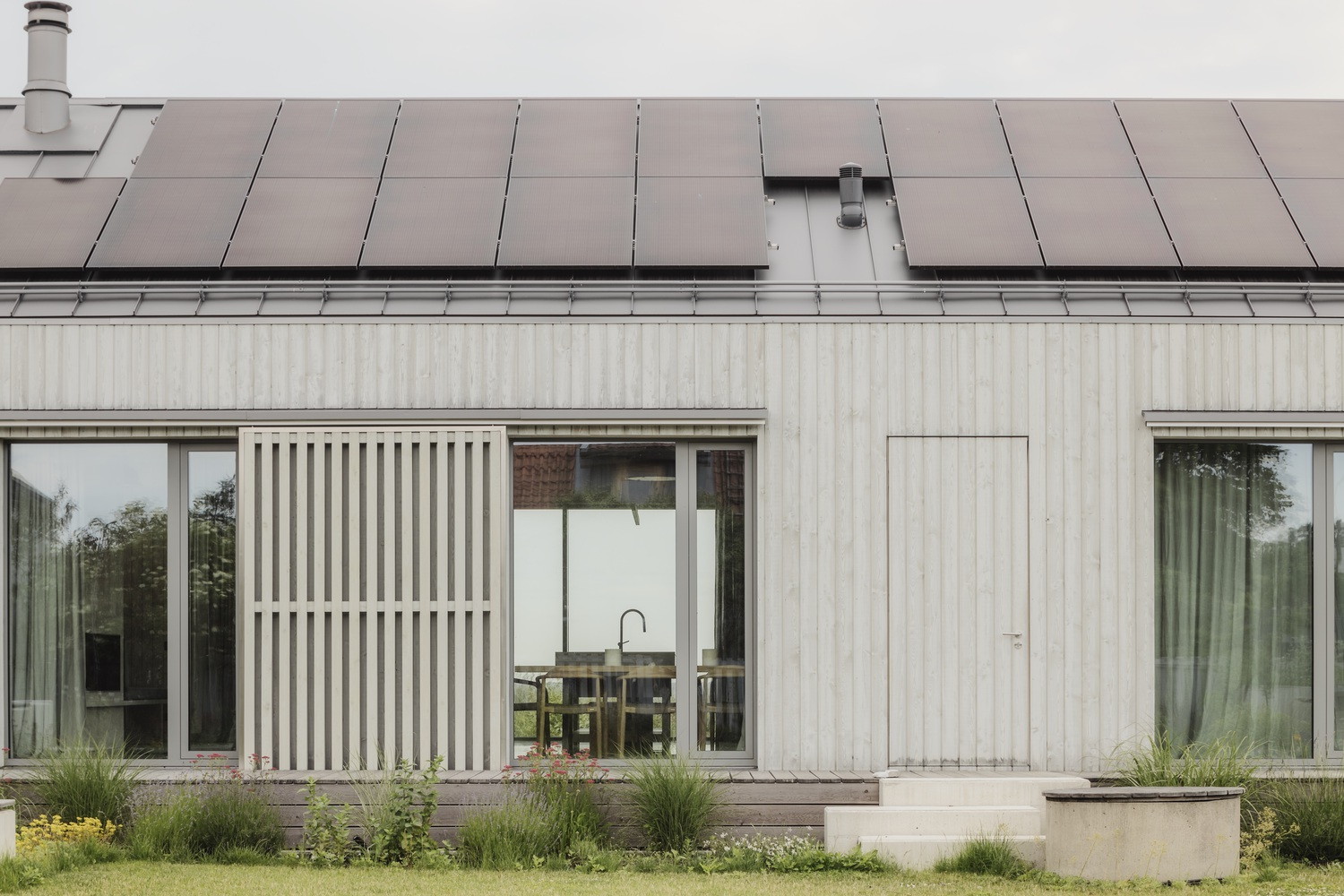 Timber facade with vertical slat screen showing interior kitchen and solar panels on standing seam roof