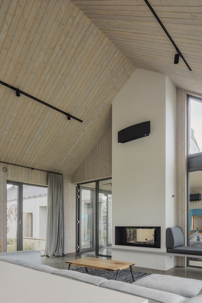 Double-height fireplace volume clad in white plaster with black track lighting on timber ceiling