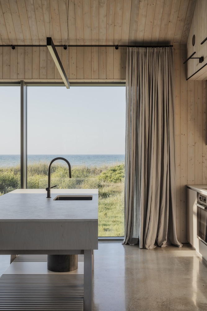 Kitchen island with integrated sink framed by timber walls and curtains with ocean horizon visible beyond